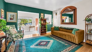 A living room with a teal wall, a patterned rug, a brown sofa, and a wooden bookshelf.