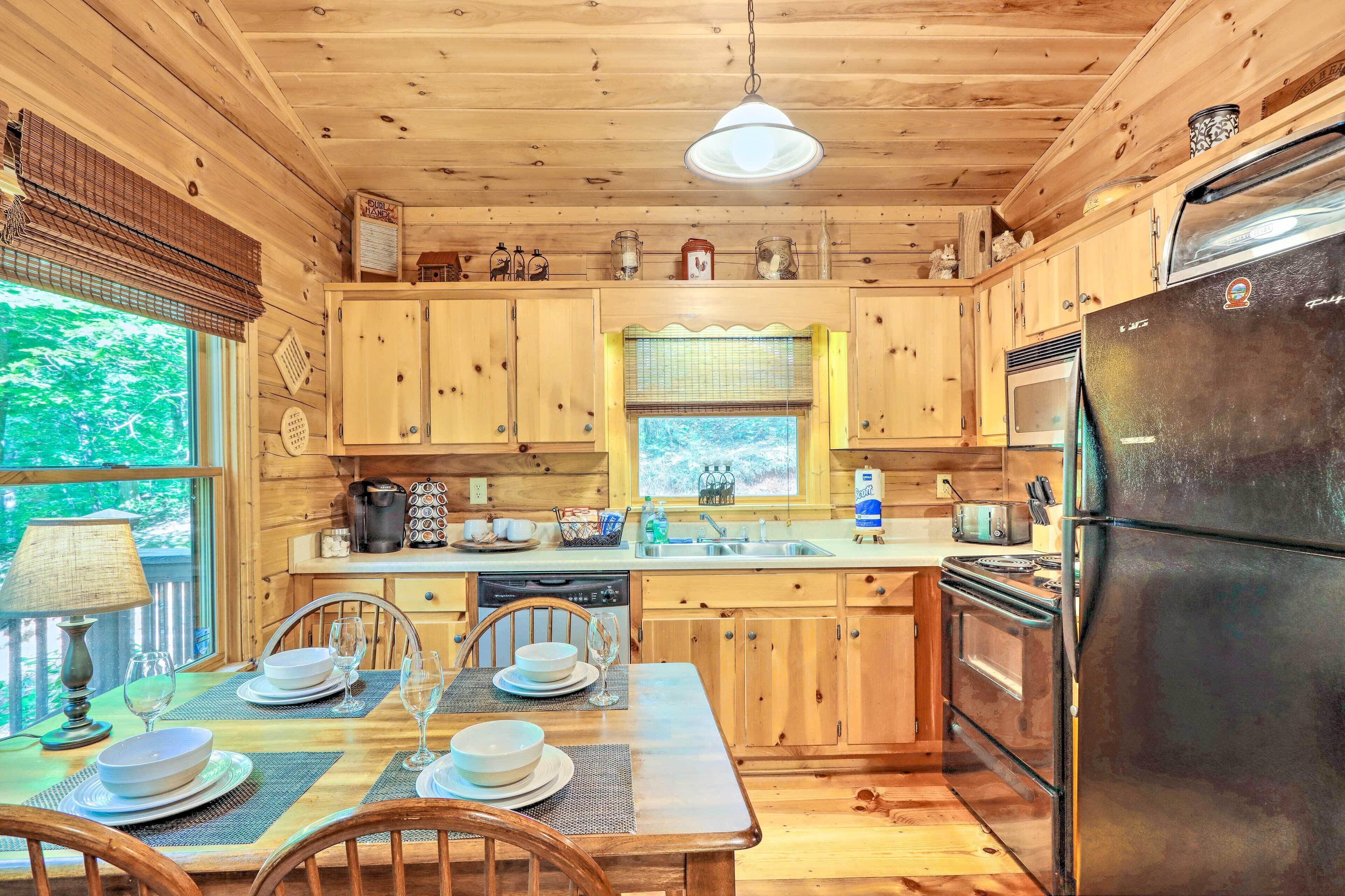 A wooden cabin kitchen with a dining table set for four, a refrigerator, and a window overlooking greenery.