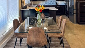Una cocina moderna con armarios oscuros, electrodomésticos de acero inoxidable y una mesa de comedor de vidrio con sillas marrones.