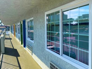 A covered outdoor area with a row of windows overlooking a parking lot and buildings. - Bposhtels Anaheim (Anaheim)