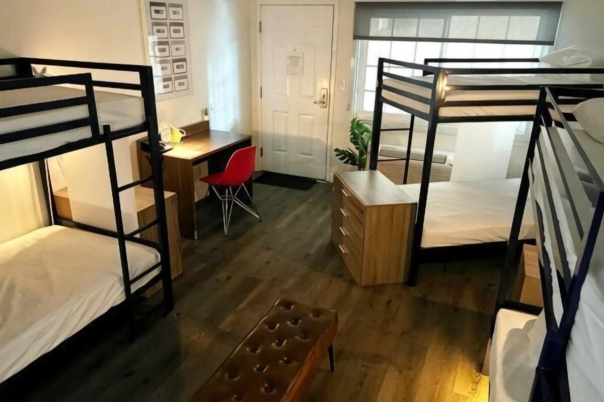 Une chambre de dortoir avec des lits superposés, un bureau, une chaise rouge et un petit banc.