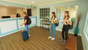 A reception area with a counter, a bench, and a window. - Bposhtels Anaheim (Anaheim)