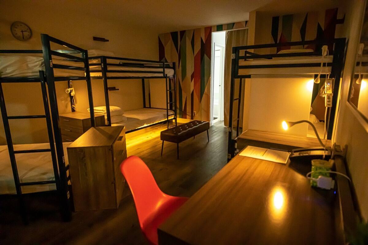 Une chambre de dortoir avec des lits superposés, un bureau en bois, une chaise rouge et une lampe.
