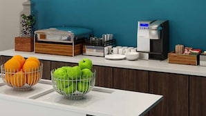 A breakfast bar with a coffee machine, fruit bowls, and a buffet area. - Bposhtels Anaheim (Anaheim)