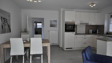 Eine moderne Küche mit weißen Schränken, einem eingebauten Backofen und einer Mikrowelle. Es gibt einen Essbereich mit einem Holztisch und zwei weißen Stühlen.