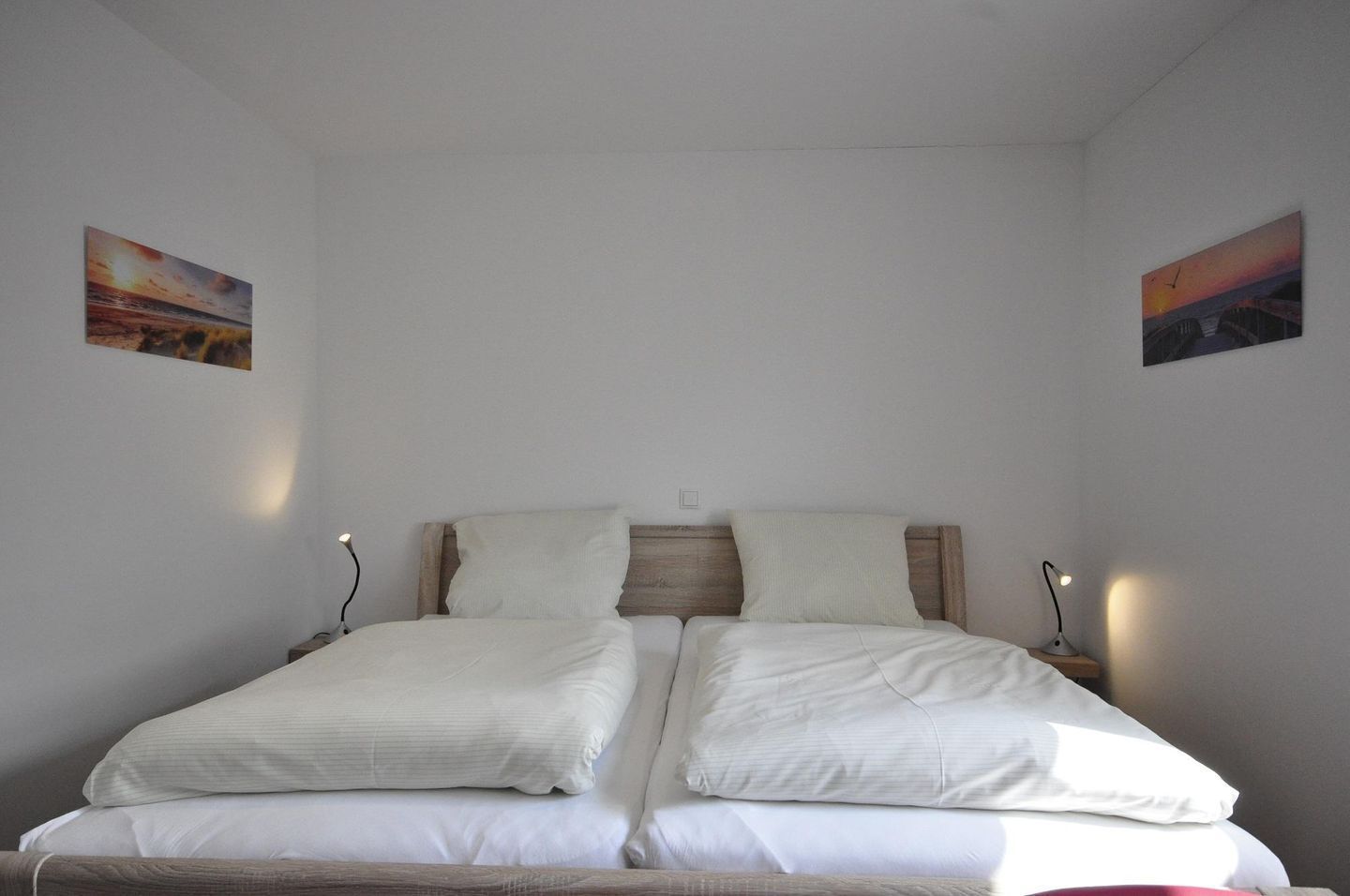 Ein Doppelbett mit zwei Kissen, einem Holzkopfstück und Nachttischlampen.