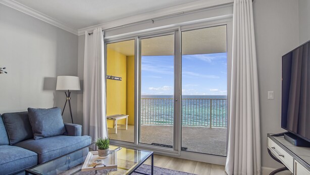 Un salon moderne comprenant un canapé, une table basse, un téléviseur et un balcon offrant une vue sur l’océan.