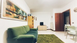 A living room with a green sofa, a painting, a television, and a dining area with chairs. - Holiday Properties Terni Central Apartment (Terni)
