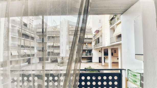 A balcony with a view of a residential area, featuring a black railing with circular cutouts and a sheer curtain partially covering the window. - Holiday Properties Terni Central Apartment (Terni)