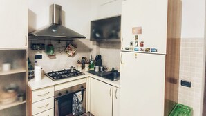 A compact kitchen with a gas stove, oven, and stainless steel range hood. There is a microwave above the stove, a sink, and a refrigerator. - Holiday Properties Terni Central Apartment (Terni)