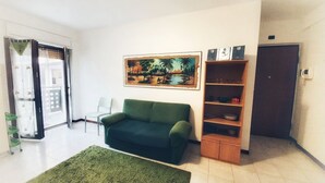 A living room with a green sofa, a painting, a wooden cabinet, and a door. - Holiday Properties Terni Central Apartment (Terni)