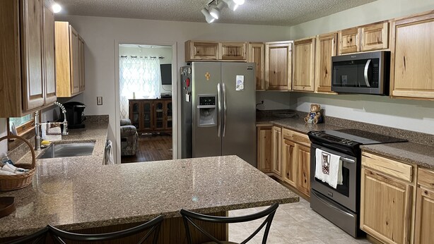 A kitchen with granite countertops, wooden cabinets, stainless steel appliances, and a central island with bar stools. - Mamaws mountain view Quiet country setting in the middle of a lot of attractions (Fletcher)