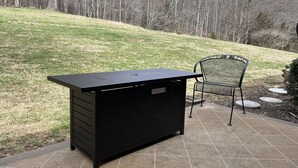 A black outdoor storage unit with multiple drawers, a metal chair, and a paved patio area with a grassy hill in the background. - Mamaws mountain view Quiet country setting in the middle of a lot of attractions (Fletcher)