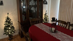 A dining area with a red tablecloth, two Christmas trees, a cabinet with dishes, and a window with blinds. - Mamaws mountain view Quiet country setting in the middle of a lot of attractions (Fletcher)