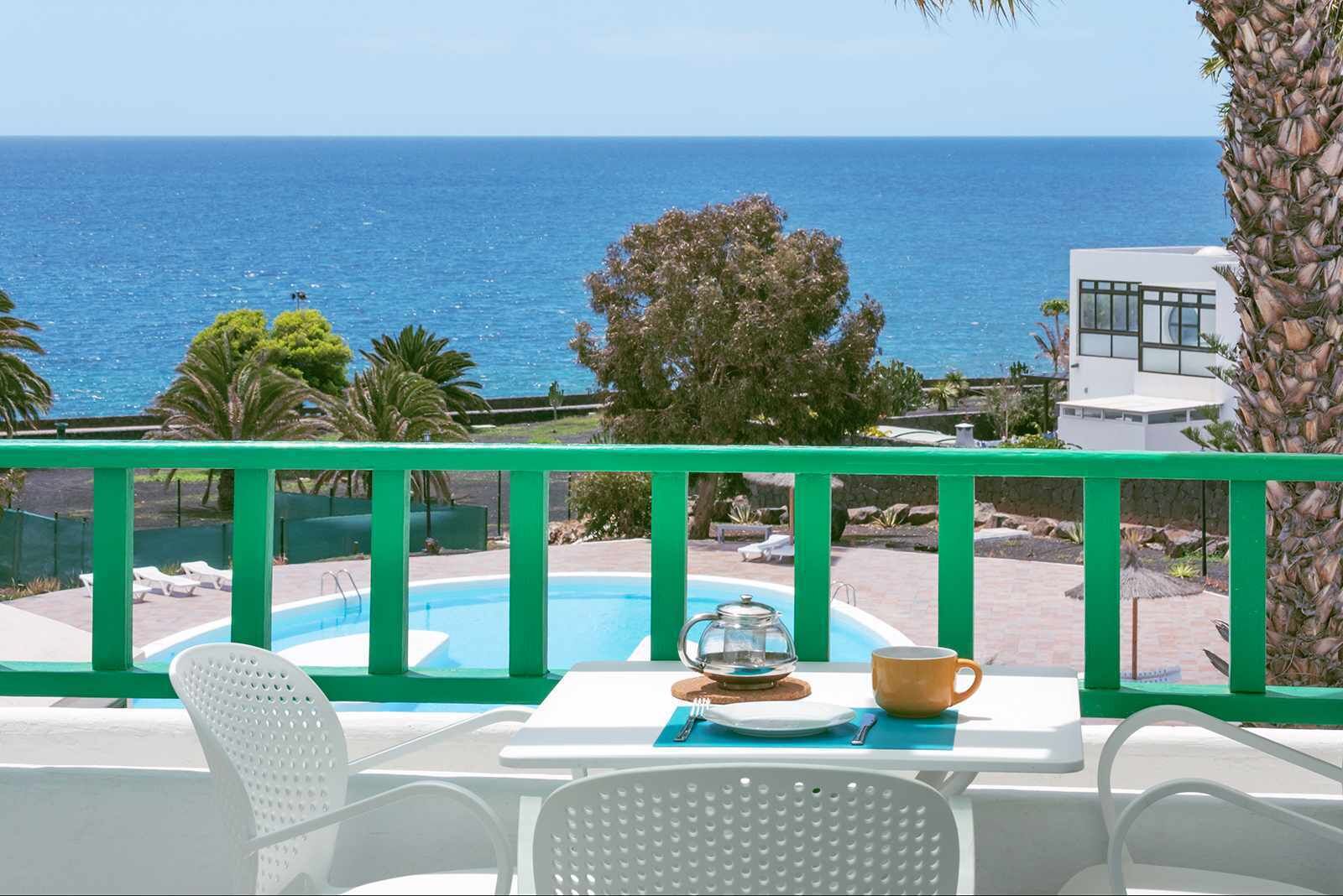 Ein Balkon mit Meerblick, ein Schwimmbad und ein Tisch mit Teekanne, Tasse und Teller.