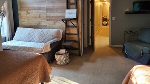 Ein gemütliches Zimmer mit Schlafkoje, einer kleinen Leiter, einem Sessel und einem Fernseher auf einem Regal.