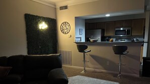 Un salon avec un canapé en cuir noir, une horloge murale décorative et un luminaire fixé au mur.