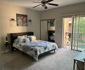 Ein Schlafzimmer mit Bett, Deckenventilator, Schreibtisch und Blick ins Freie.