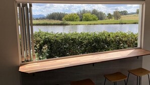 A room with a large window overlooking a lake, a wooden bench, and two stools. - Romantic lakehouse set in a private vineyard in the Hunter Valley (Lovedale)