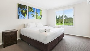 A bedroom with a large bed, a nightstand, and a window with a view of greenery. - Romantic lakehouse set in a private vineyard in the Hunter Valley (Lovedale)