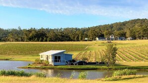 A small house with a dock by a lake, surrounded by fields and a forest in the background. - Romantic lakehouse set in a private vineyard in the Hunter Valley (Lovedale)