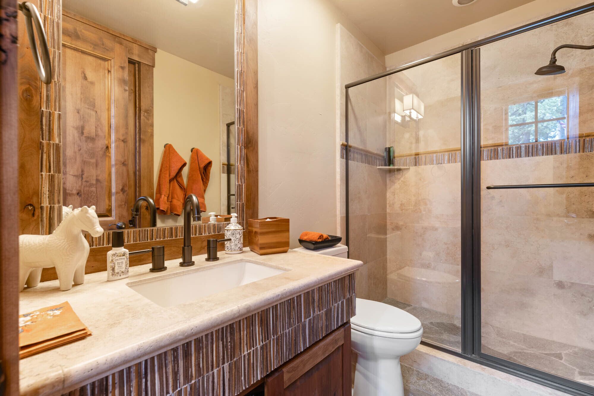 A bathroom with a wooden vanity, a large mirror, a glass shower enclosure, and a toilet.