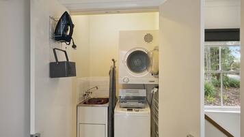 A compact laundry room with a washing machine, dryer, and ironing station.