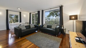 A modern living room with two black sofas, a wooden dining table, and large windows with curtains. - 2 Bedroom Villa at Cypress Lakes Resort (Pokolbin)