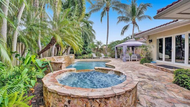Ein Garten mit Whirlpool, Schwimmbad und einer Terrasse mit Liegestühlen.