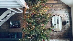 A Christmas tree in a spacious room with a wooden floor and a staircase.