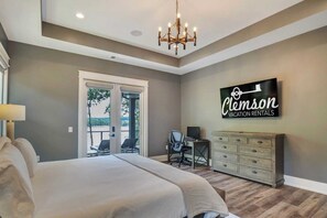 A bedroom with a large bed, a desk, a chair, a dresser, a chandelier, and a sign for vacation rentals.