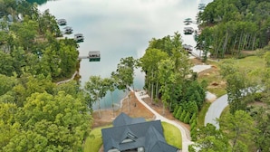 Vista aerea di una casa con un ampio vialetto, circondata da alberi rigogliosi e un lago con barche.