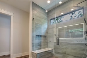 Une salle de bain moderne avec une douche Ă lâitalienne en verre, un banc et une grande fenĂȘtre.