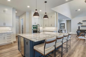 A modern kitchen with white cabinets, a large island with bar stools, and pendant lighting.