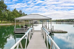 A wooden dock leading to a covered seating area with a view of a calm lake and trees.