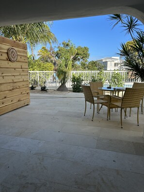 A covered patio area with a wooden wall, a round table with chairs, and a white fence. - OCEANSIDE DUCK KEY HOUSE / BOAT RAMP & DOCK  (Marathon)