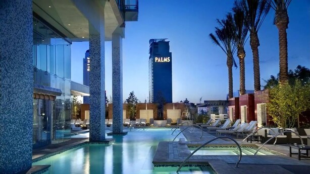 A pool area with lounge chairs, a tall building labeled "PALMS" in the background, and palm trees.