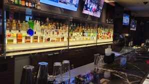 A bar area with a marble countertop, multiple liquor bottles, and two televisions mounted on the wall.