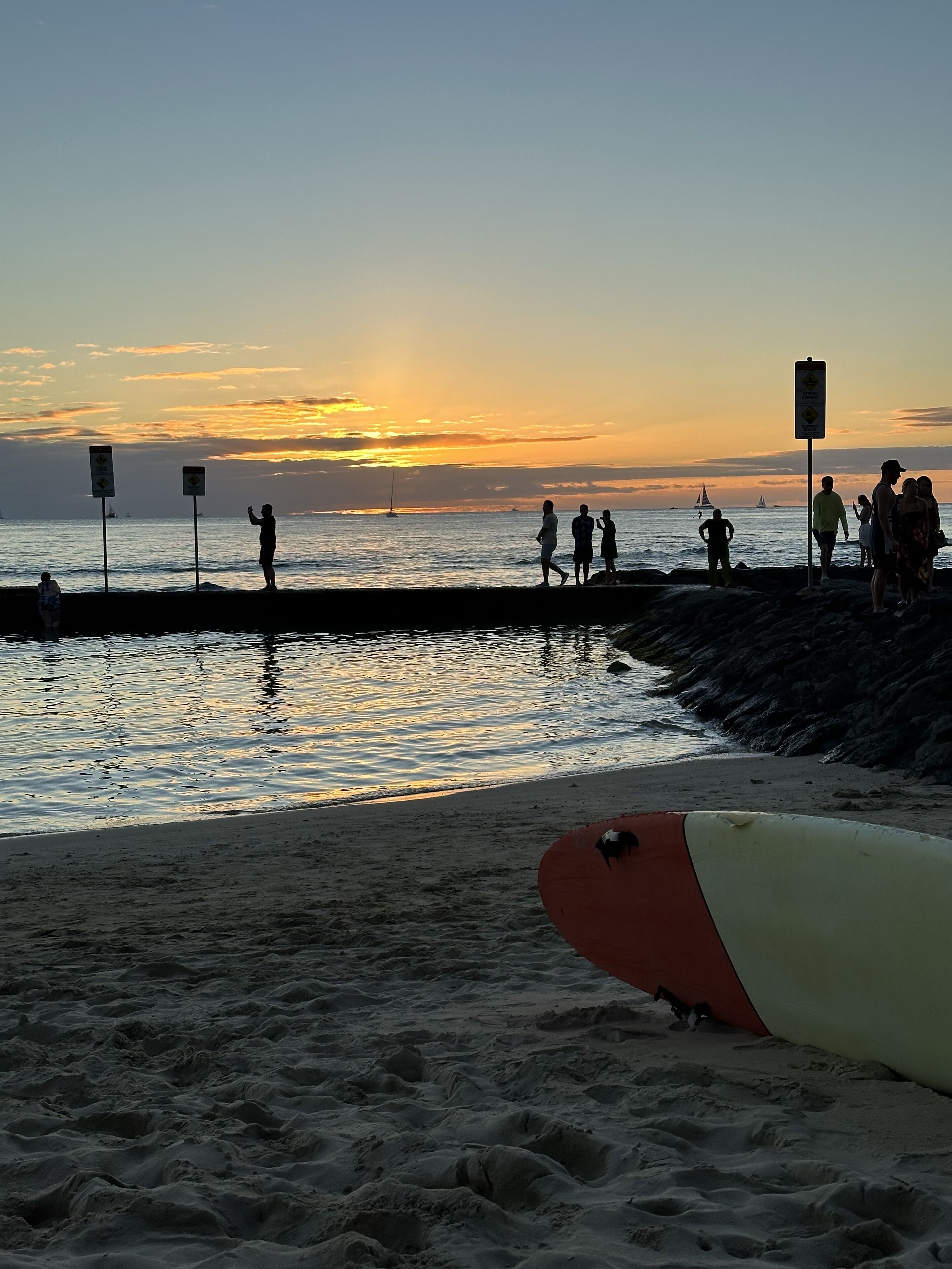 A beach scene with people and a surfboard.