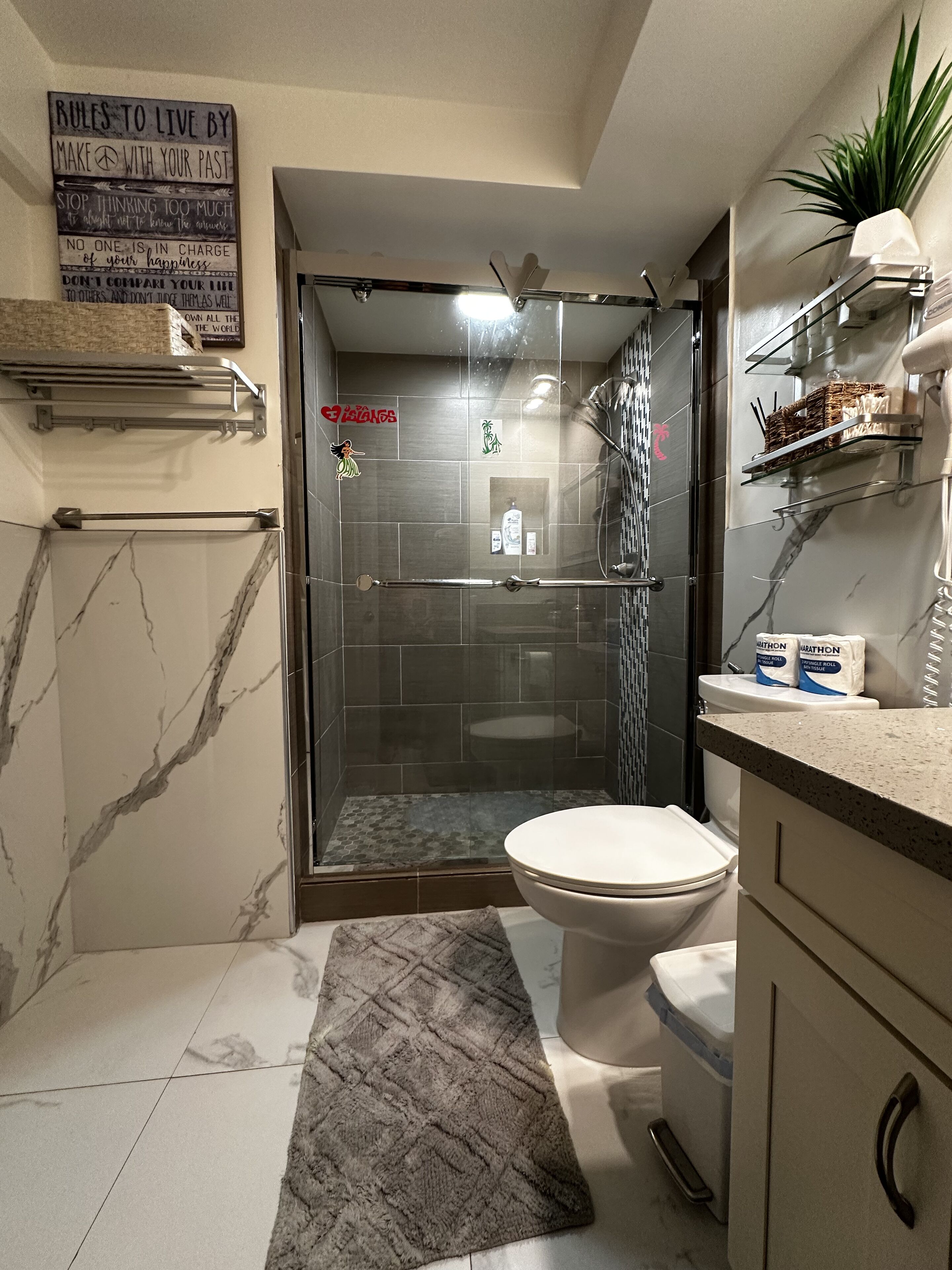 A modern bathroom with a glass-enclosed shower, a toilet, marble flooring, and a shower mat.