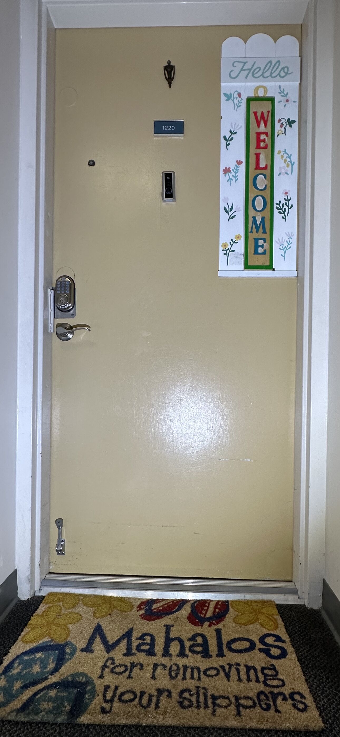 Una puerta con un cartel de bienvenida, una placa con un número y un felpudo con un mensaje.