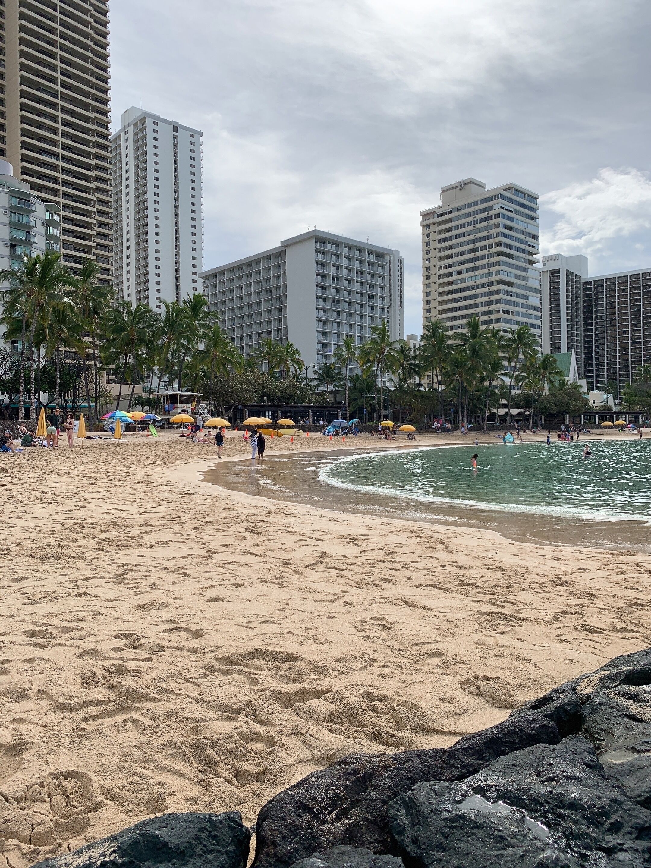 Una playa con palmeras, sombrillas y un primer plano rocoso.