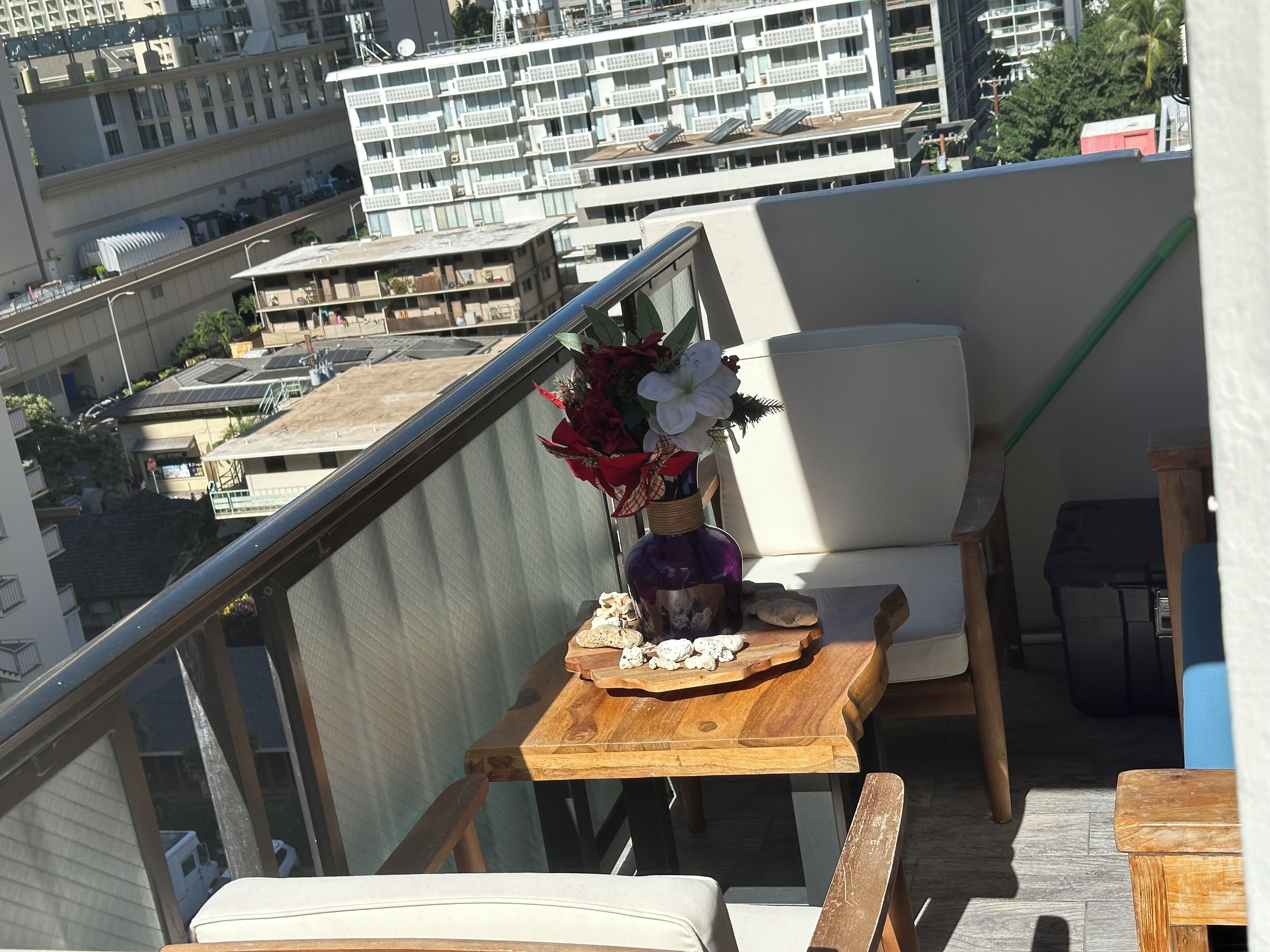 A balcony with a wooden table, a white chair, and a vase with flowers.