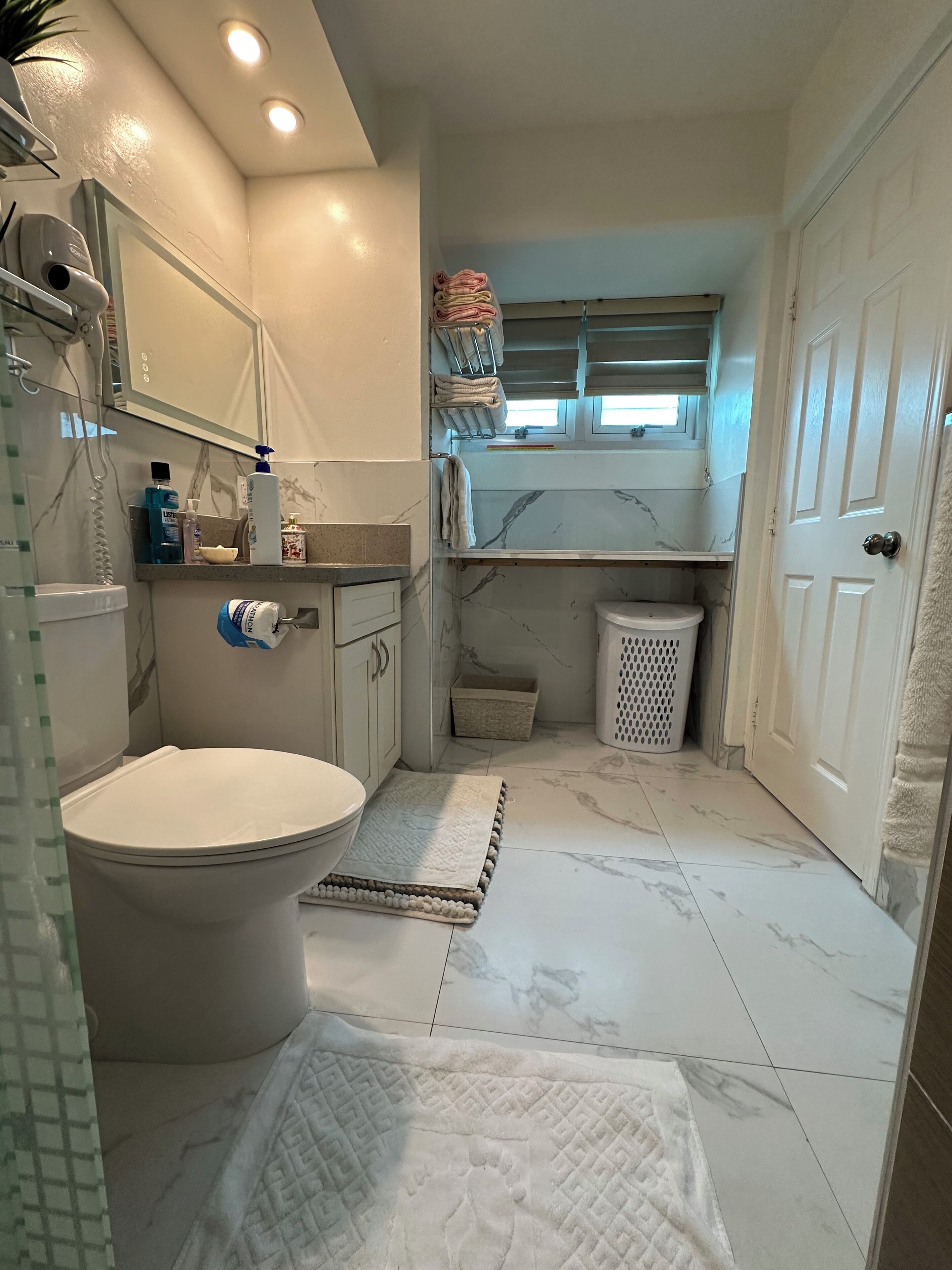 Ein kleines Badezimmer mit Toilette, Waschbecken und Spiegel. Über dem Waschbecken befindet sich ein Handtuchhalter und über der Toilette ein Fenster.