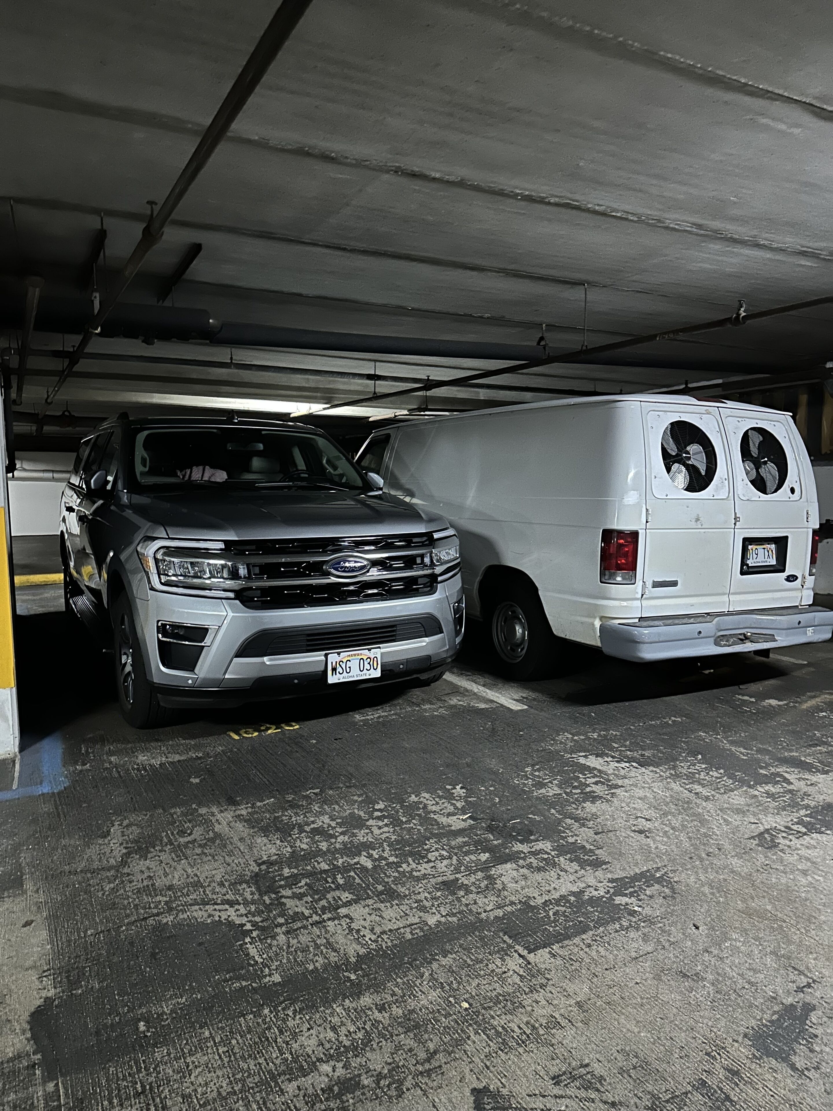 A parking garage with a silver SUV and a white van parked side by side.