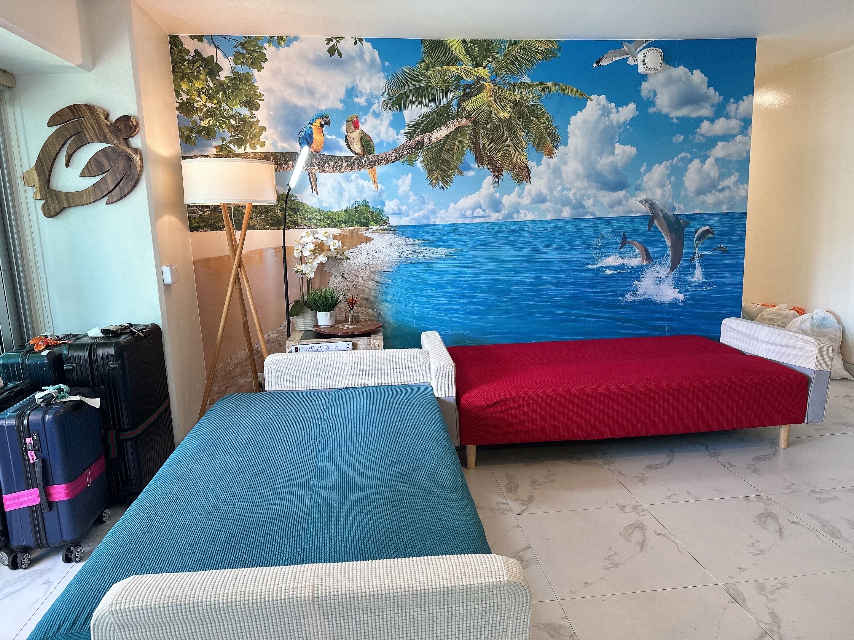 Una habitación con dos camas, un mural grande con una escena de playa y una lámpara fijada a la pared.