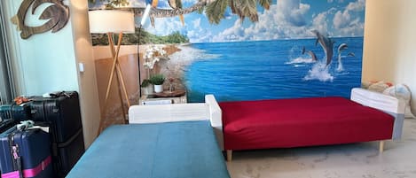 Una habitación con dos camas, un mural grande con una escena de playa y una lámpara fijada a la pared.