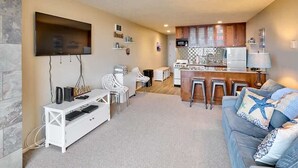 Una sala de estar moderna con un televisor de pantalla plana, un sofá, una mesa de centro y una cocina con armarios de madera y salpicadero de azulejos.