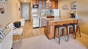 Una cocina compacta con armarios de madera, una isla central con taburetes, un microondas y un refrigerador.