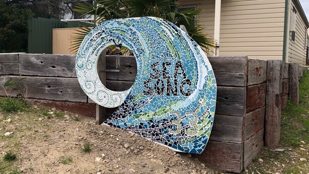 A mosaic sign with the text "SEA SILENCE" in front of a house with a balcony.